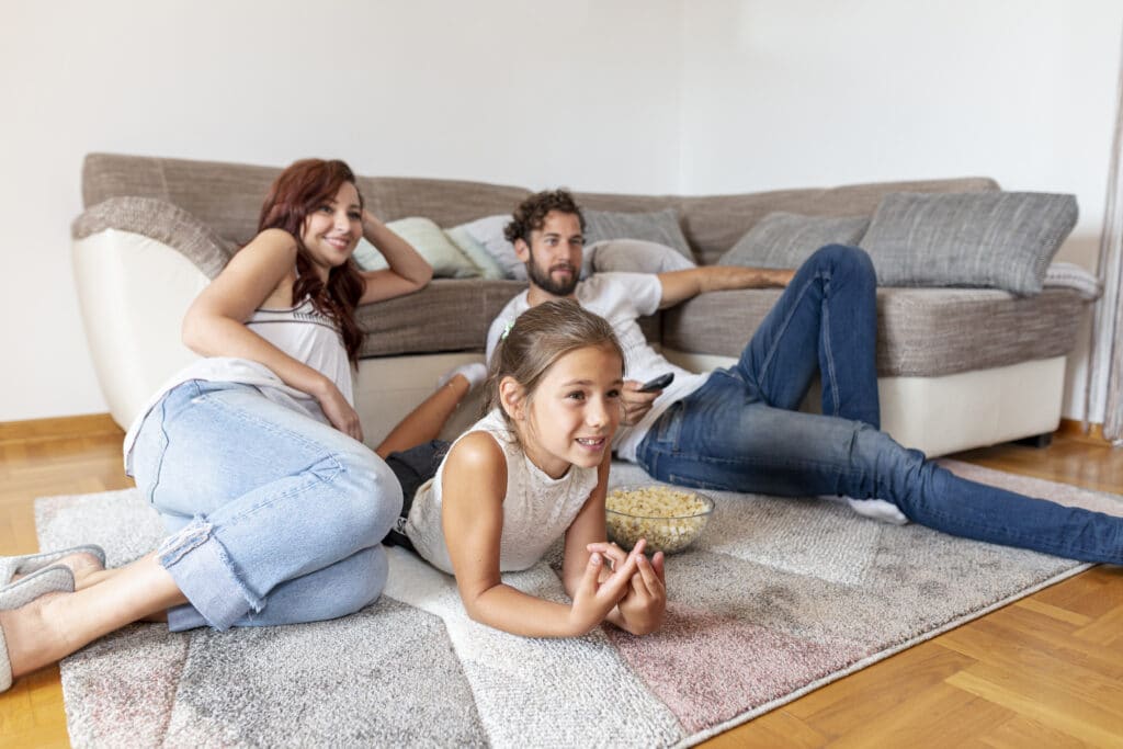 A family consisting of mother, father and daughter sitting on the carpet in a room.  Illustration of the text how to wash fur carpet.