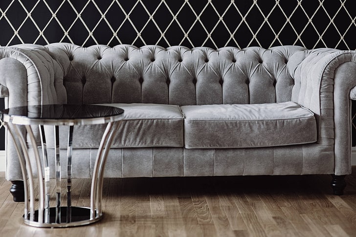 Gray velvet sofa with glass table and wooden floor. 