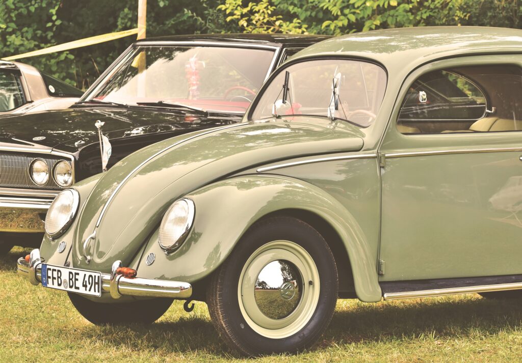 Image of a green beetle in the foreground and a black vintage car in the background. 