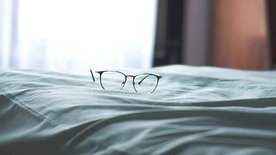 Imagem de um óculos em cima de uma cama. Ilustração do texto lavar sofá em Promissão.