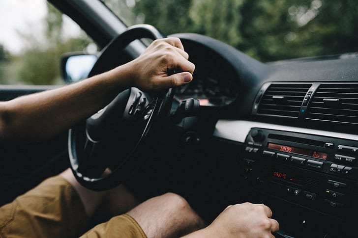 Imagem de uma pessoa sentada no interior de um veículo, segurando o volante. Ilustração do texto carro cheiroso.