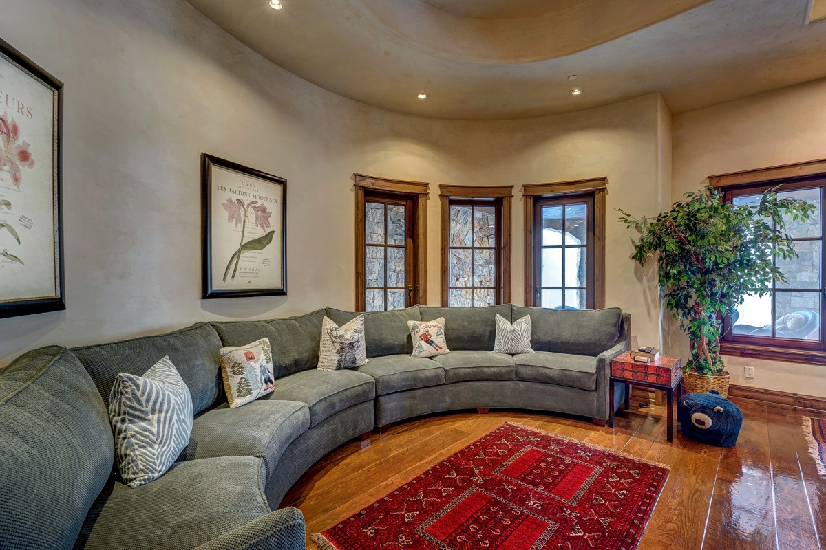 Imagem de uma sala de estar ampla com sofá com vários lugares, piso de madeira e três janelas. Ilustração do texto sobre como tirar mancha do sofá