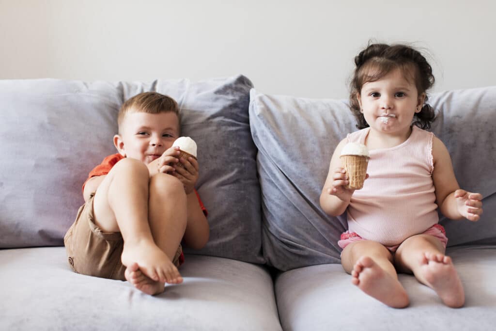 duas crianças sentadas em um sofá com um sorvete na mão de cada uma. imagem ilustrativa de texto sobre limpar sofá centro americana.