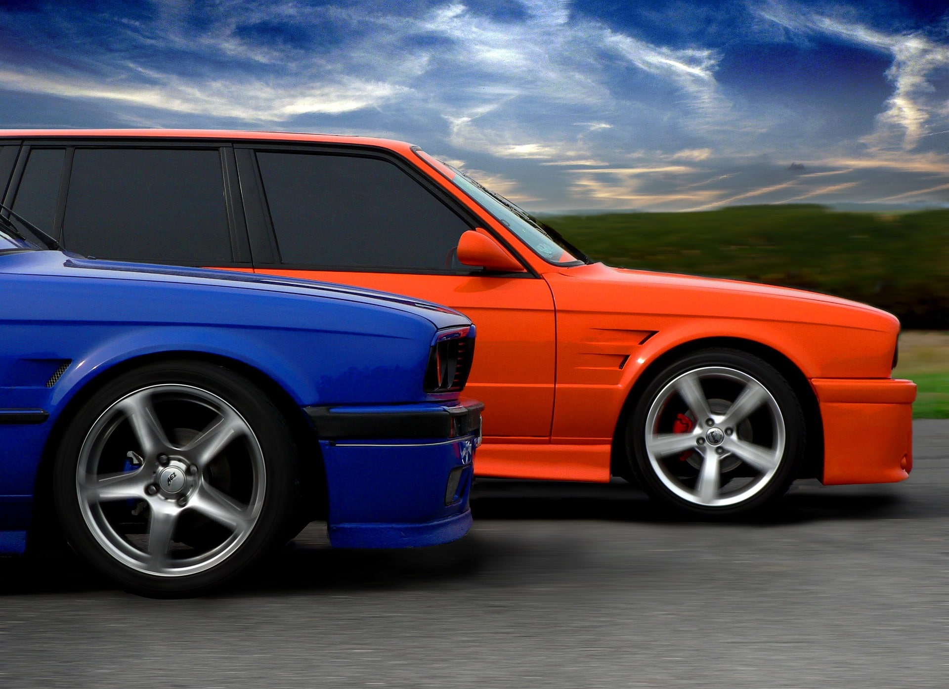 Frente de carros azul e laranja, em estrada com tempo nublado.