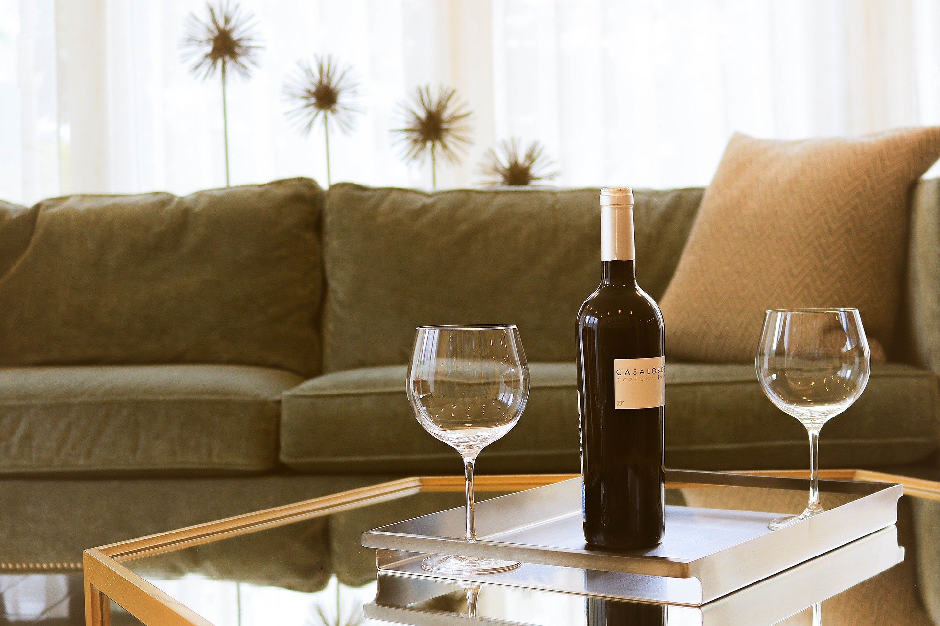 Garrafa de vinho e duas taças na mesa de centro e um sofá marrom ao fundo. Imagem de texto sobre como tirar mancha de vinho.Imagem do conteúdo lavar sofá na Chapada dos Guimarães.