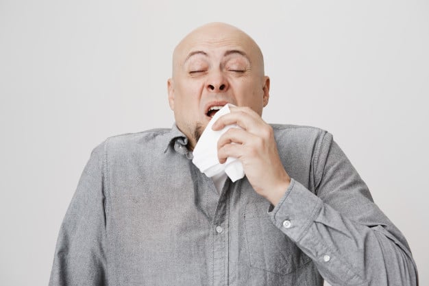 Homem careca espirrando com um lenço branco no nariz. Imagem ilustrando texto limpeza de colchão em Tocantins.