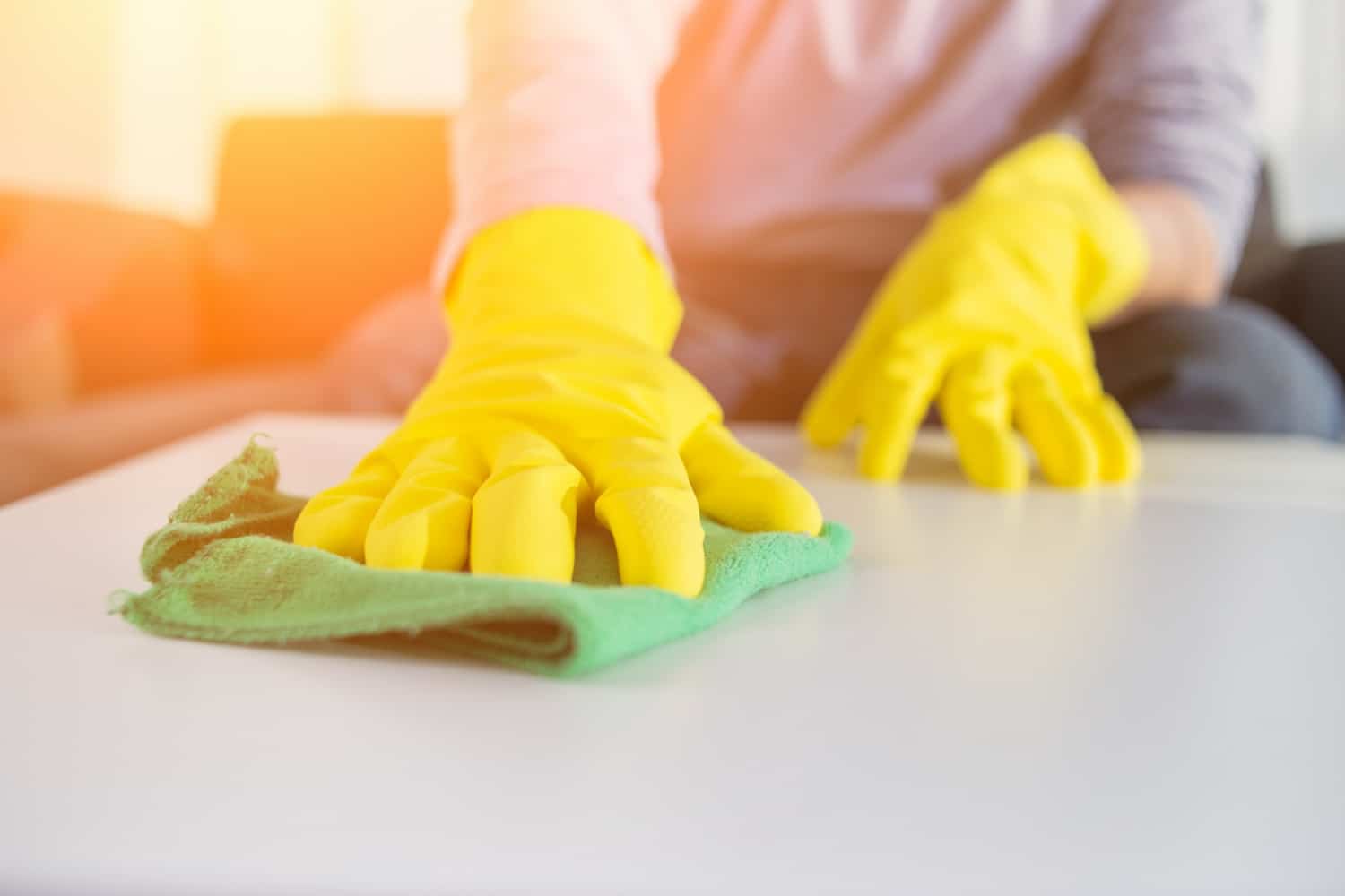 Pessoa com luvas amarelas higieniza uma superfície branca com o auxílio de um tecido verde. Ilustração do texto sobre limpeza profissional na Paralela.