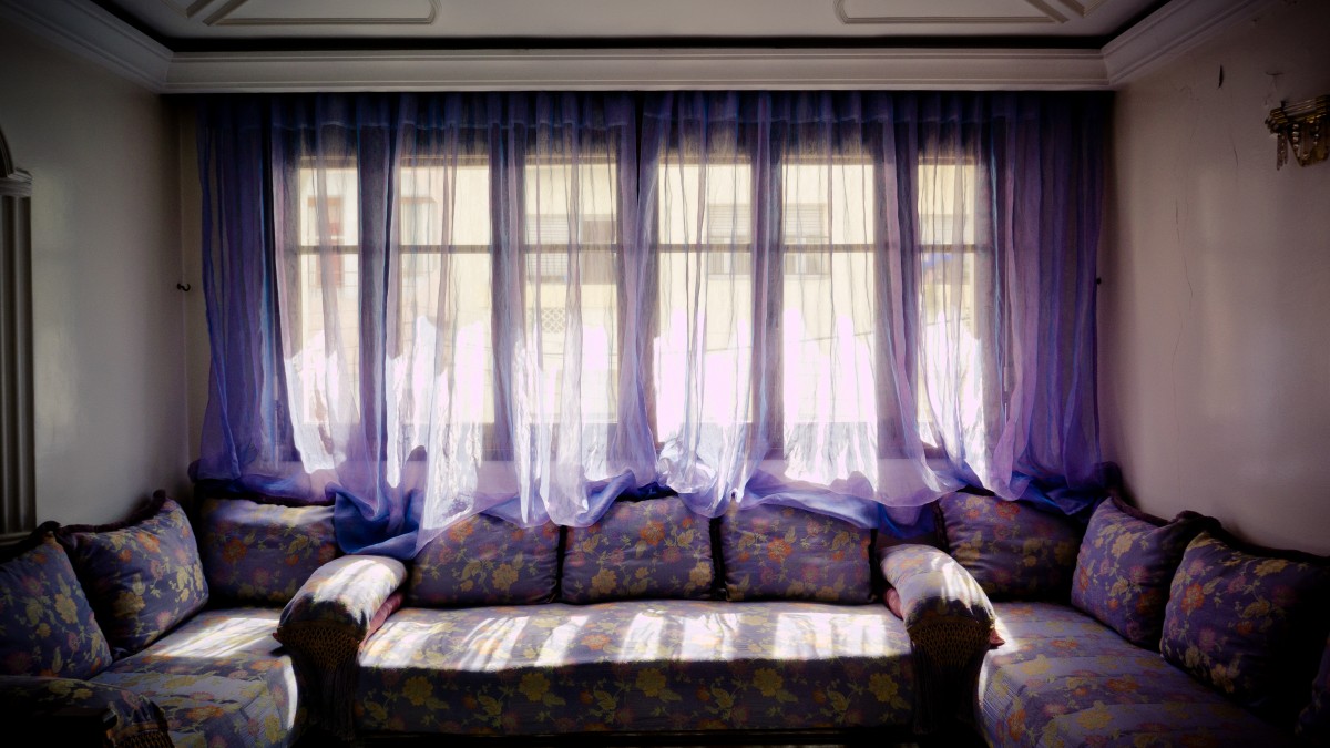 Sala de estar com cortinas roxas, sofas e almofadas roxas, com temas florais. Imagem do conteúdo sobre lavagem a seco de sofá.