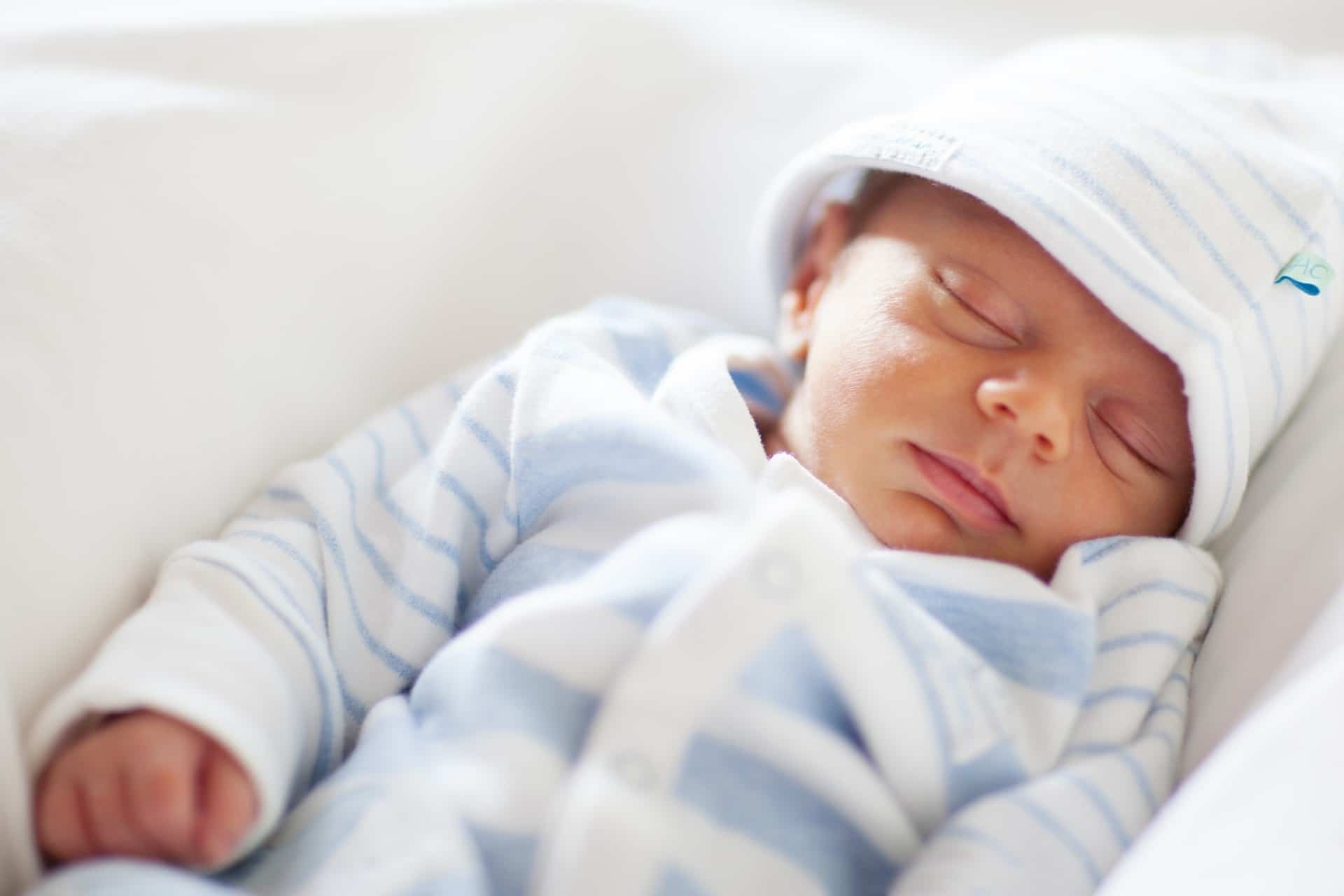 Bebê dormindo com touca e roupa listrada. Imagem ilustrativa texto limpar vômito sofá.