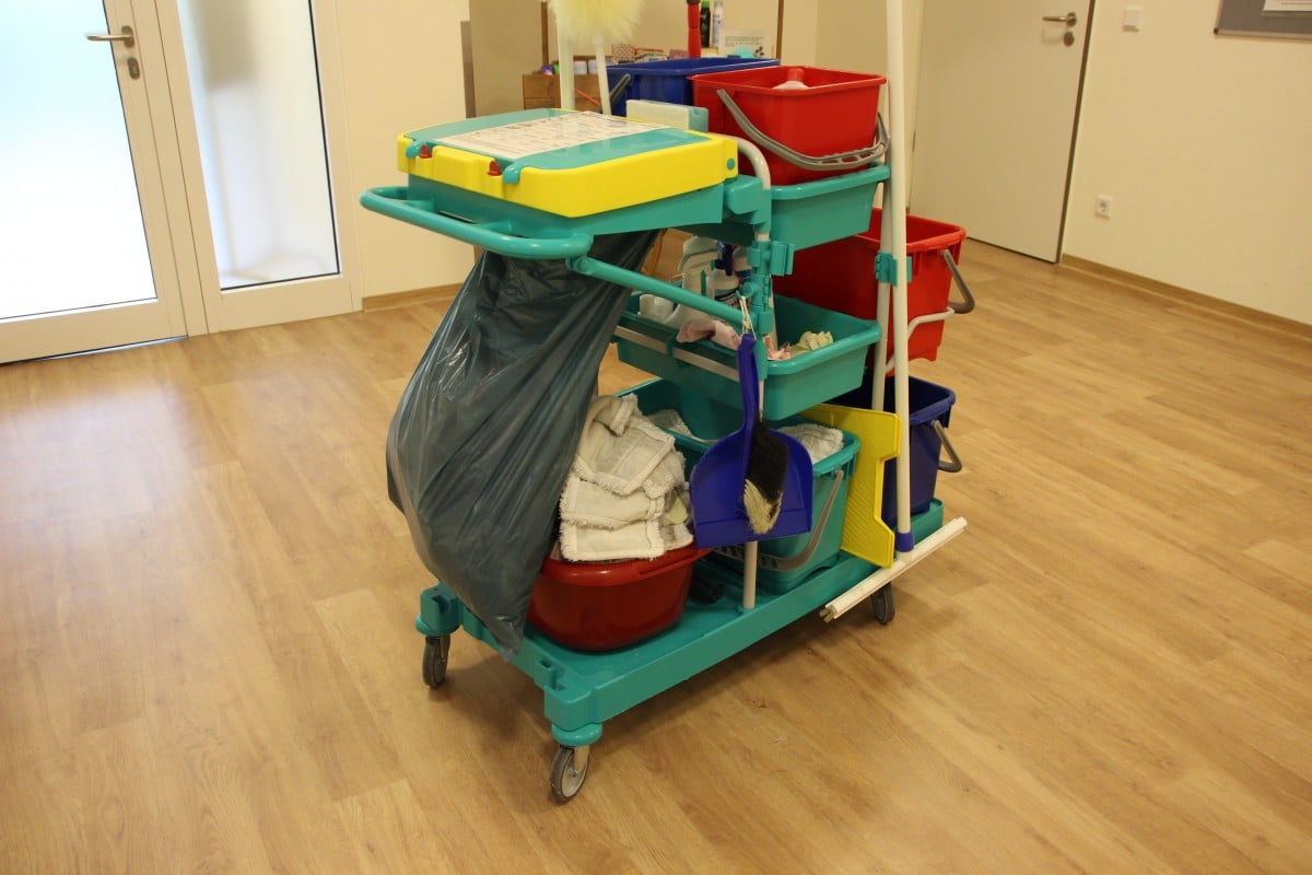 Carrinho em piso de madeira, com panos, vassoura, rodo, bacia, baldes, cestos e produtos de limpeza. Imagem do conteúdo lavar sofá Centro Juazeiro.