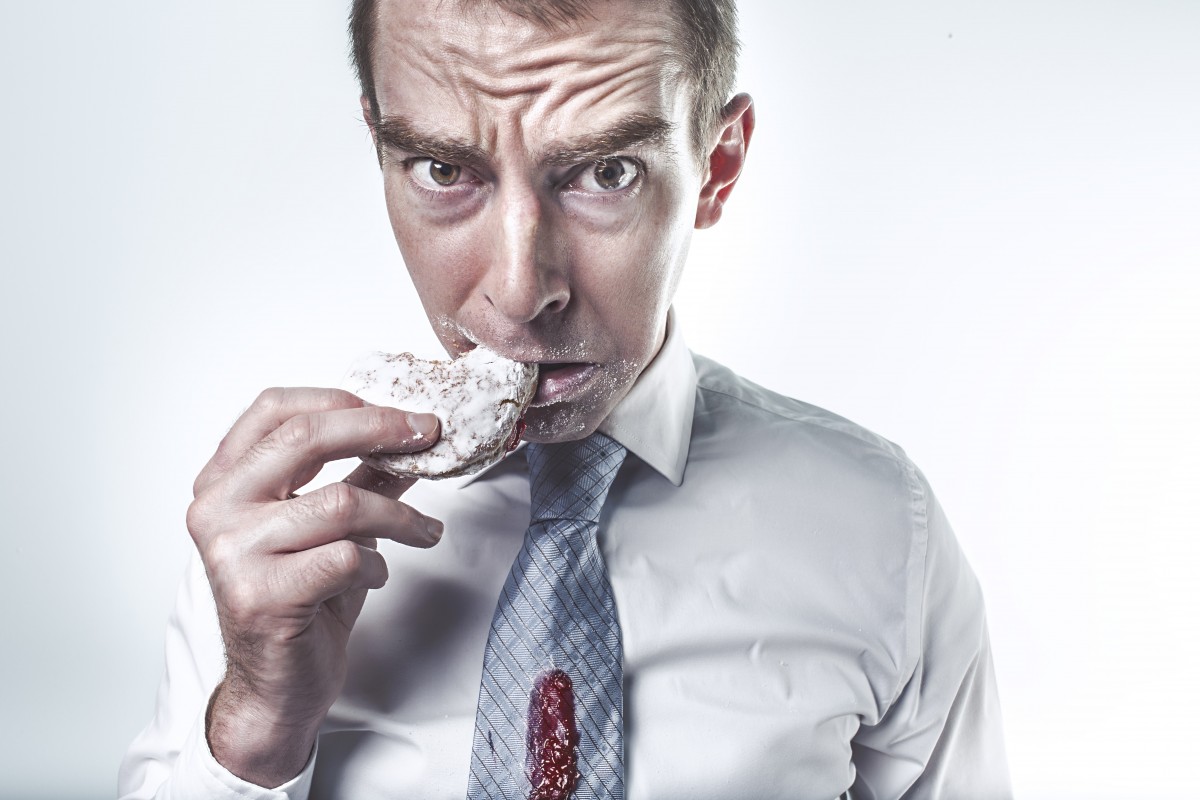 Homem comendo, com gravata manchada. Imagem do conteúso sobre como tirar mancha de roupa.