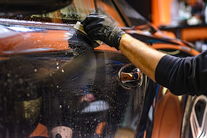 Waxing black car door, with glove and sponge.  Illustrative image text waxing car.