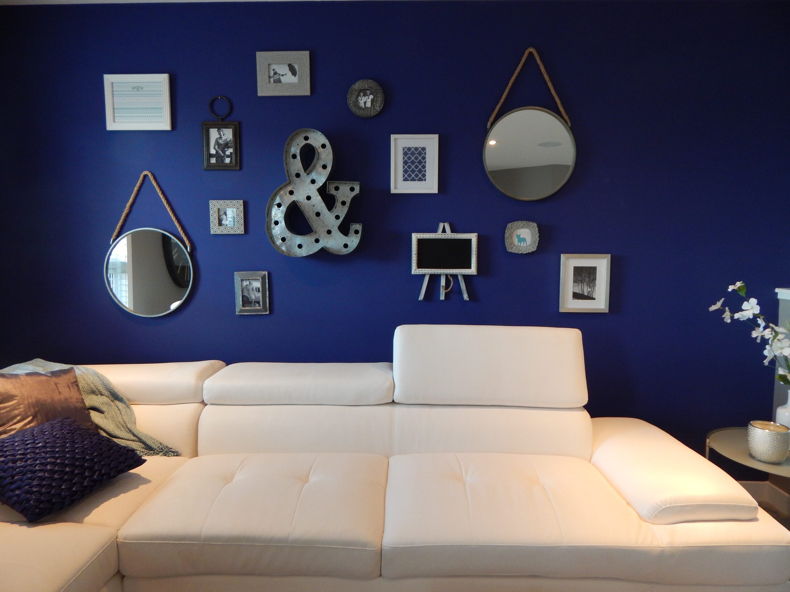 Sofá branco e parede azul com quadros, espelhos e itens de decoração. Imagem ilustrativa texto