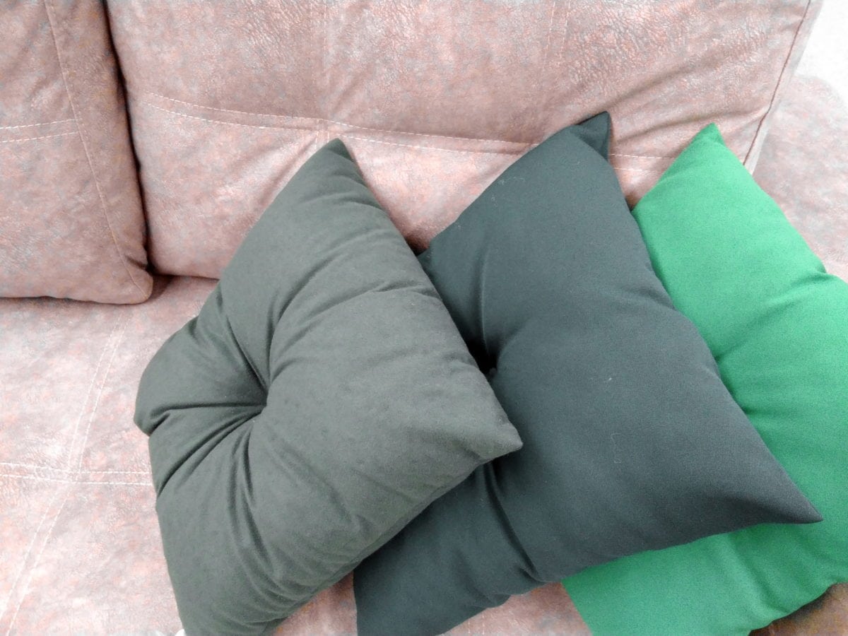 Travesseiros cinza, chumbo e verde em sofá rosa. Imagem ilustrativa texto