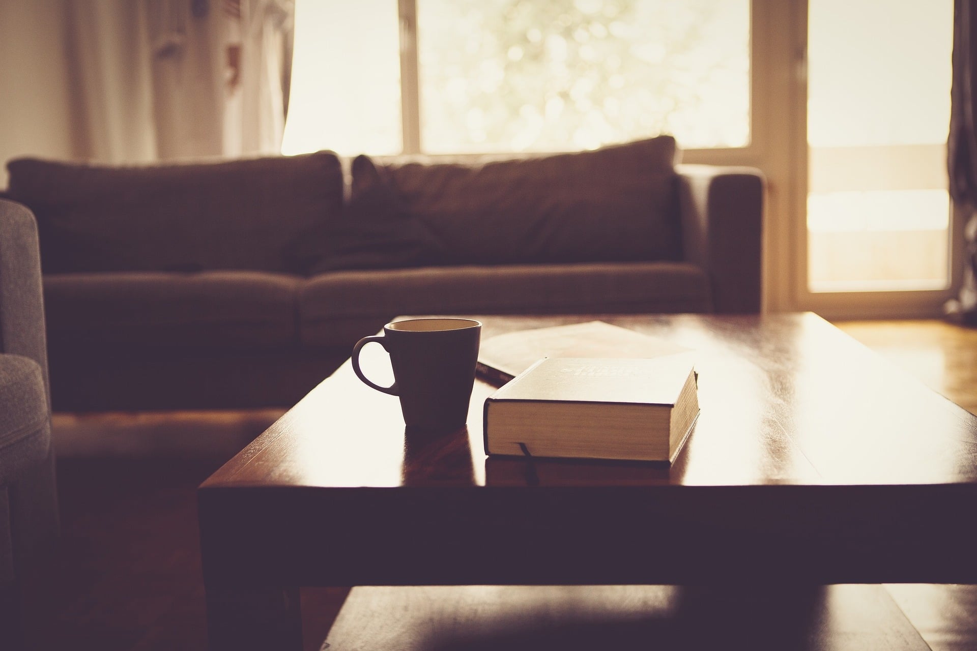 Sala com mesa de centro, com xícara e livro, sofá ao fundo. Imagem ilustrativa texto