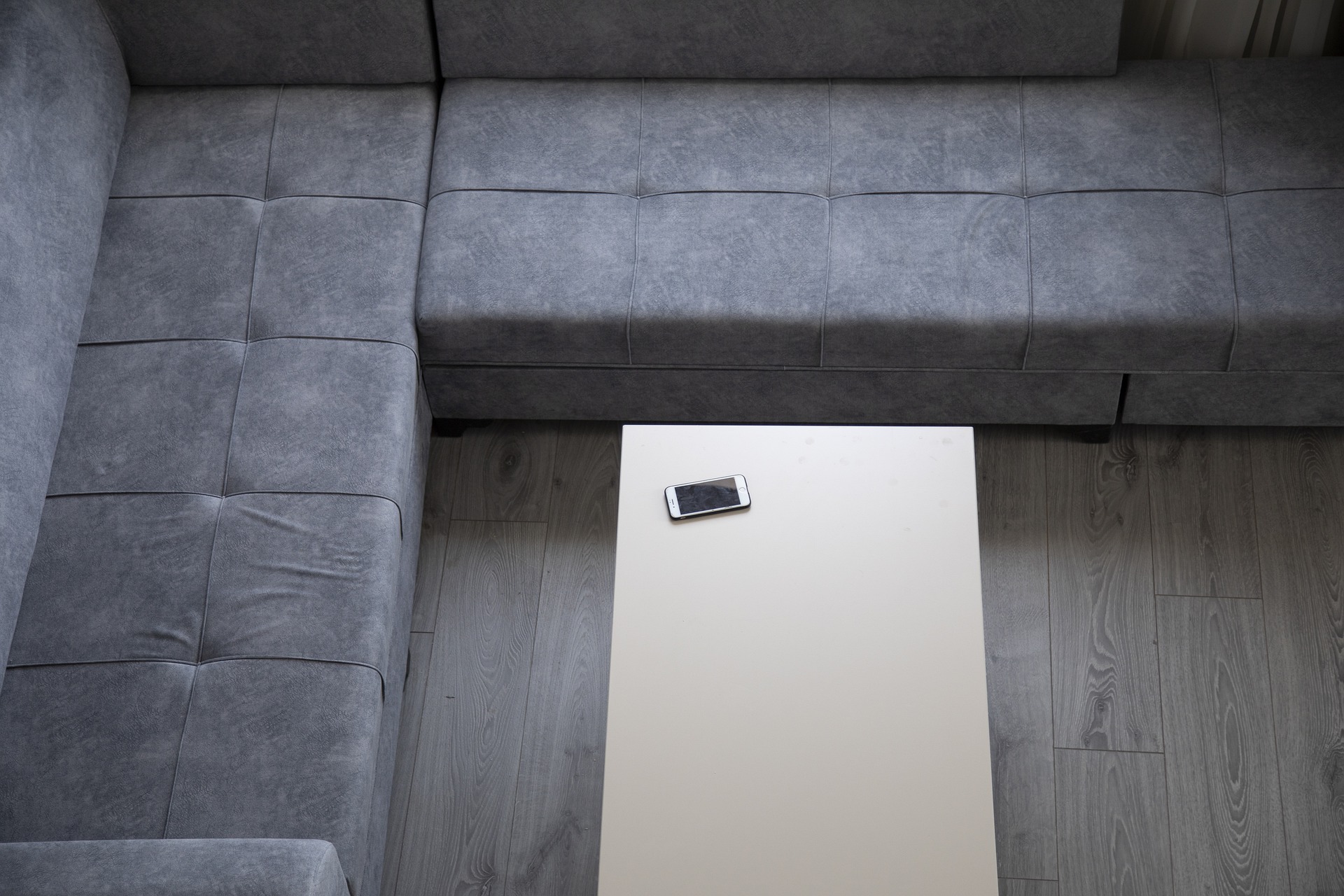 Sofá de canto cinza, visto de cima. Mesa com celular. Iagem ilustrativa texto