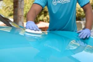 Pessoa usando luvas polindo o capo de um carro azul. Ilustração do texto sobre polimento espelhado.