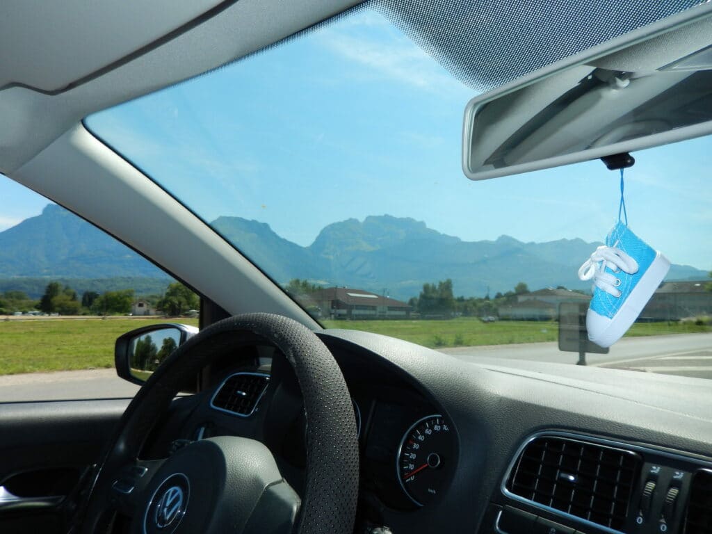 Visão interna do veículo da Volkswagen. Sapatinho no retrovisor e montanhas ao fundo. Imagem do conteúdo como limpar os vidros do carro.