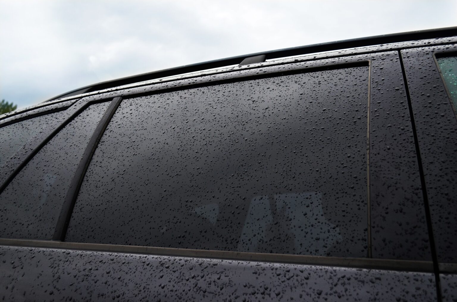 Chuva no vidro lateral com insulfilm. Imagem ilustrativa texto como limpar os vidros do carro.