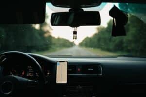 Vista interna de um carro em uma estrada com árvores verdes. Ilustração do texto sobre como limpar parabrisas.