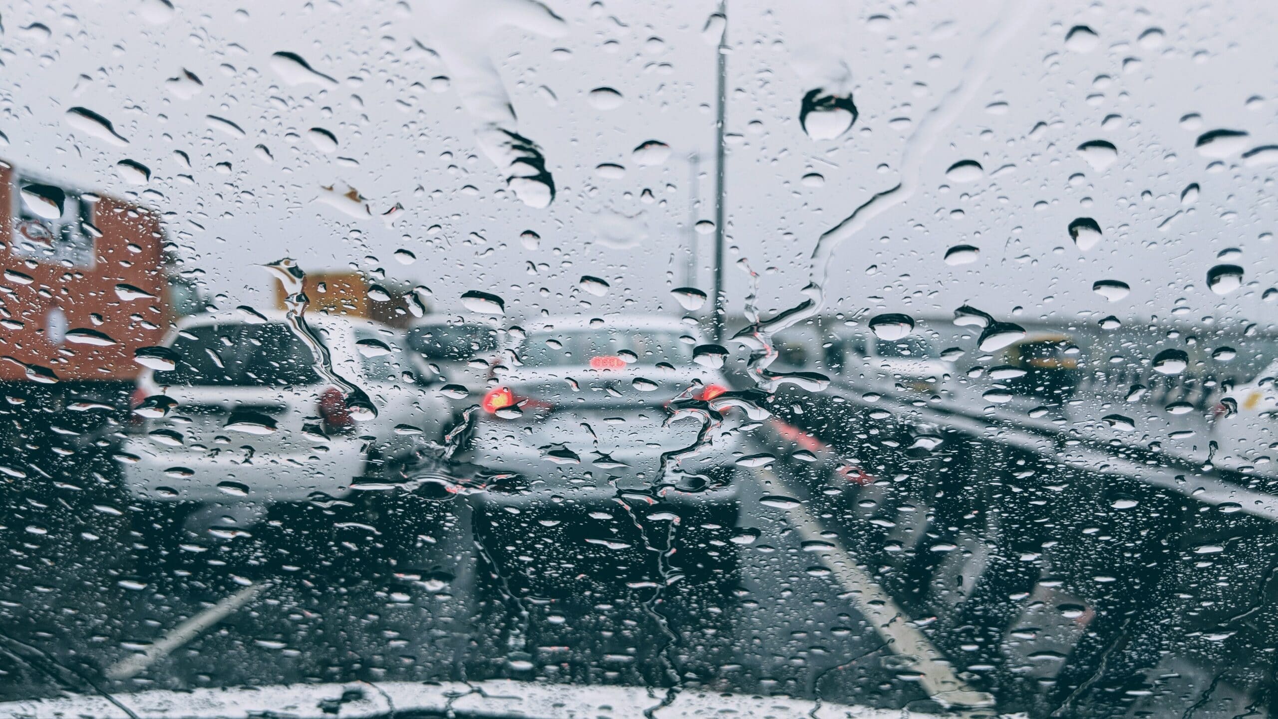 Imagem do interior de um veículo. A vista é de uma para-brisa molhado e o trânsito. Ilustração do texto sobre como limpar parabrisa.