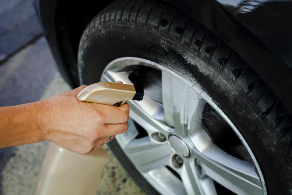 Hand holding a spray bottle while cleaning a car wheel.  Illustrative image for the text ecological washing.