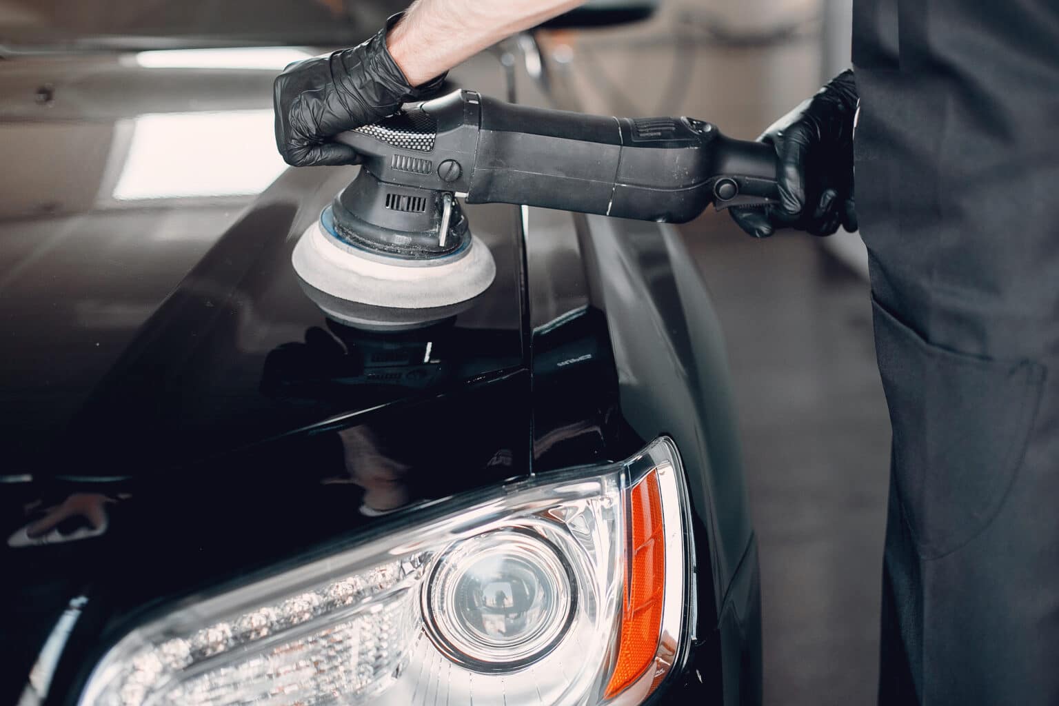 Pessoa usa um dispositivo elétrico de polir para cuidar da lataria de um carro preto. Ilustração do texto sobre para que serve o polimento.