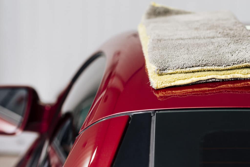 Shaggy gray cloth on the roof of a red car.  Illustrative textIllustration of the text on car polishing in BH.