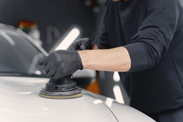 Homem fazendo o polimento do capô de um carro branco. Imagem ilustrativa do texto sobre técnicas de polimento.