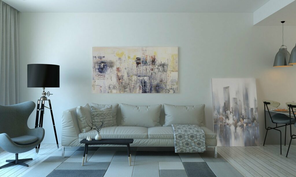Sofá branco de três lugares, um tapete quadriculado no chão e um quadro de arte na parede branca ao fundo. Imagem do texto sobre como limpar casa.