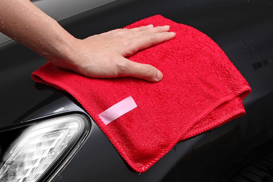 Pano de microfibra vermelho em um carro preto. Imagem do conteúdo como tirar risco de carro.