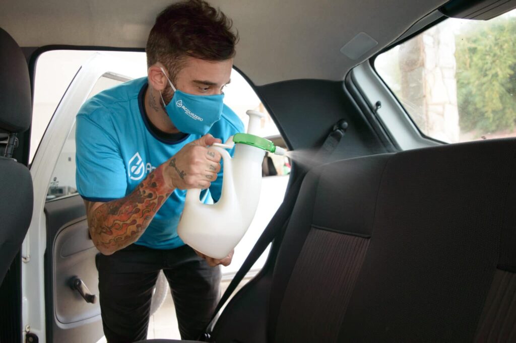 Man wearing a blue shirt and mask, sanitizes the interior of a vehicle with the aid of a spray bottle.  Illustration of the text clean sofa Brada Alto.