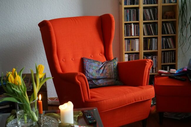 Poltrona vermelha em uma sala de estar com parede e almofadas no tom cinza. Ilustração do texto sobre como limpar estofado de cadeira.