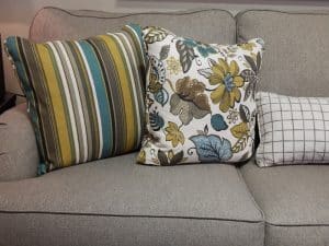 Imagem de parte de um sofá na cor cinza com almofadas coloridas sobre ele. Imagem ilustrativa texto lavagem e impermeabilização.