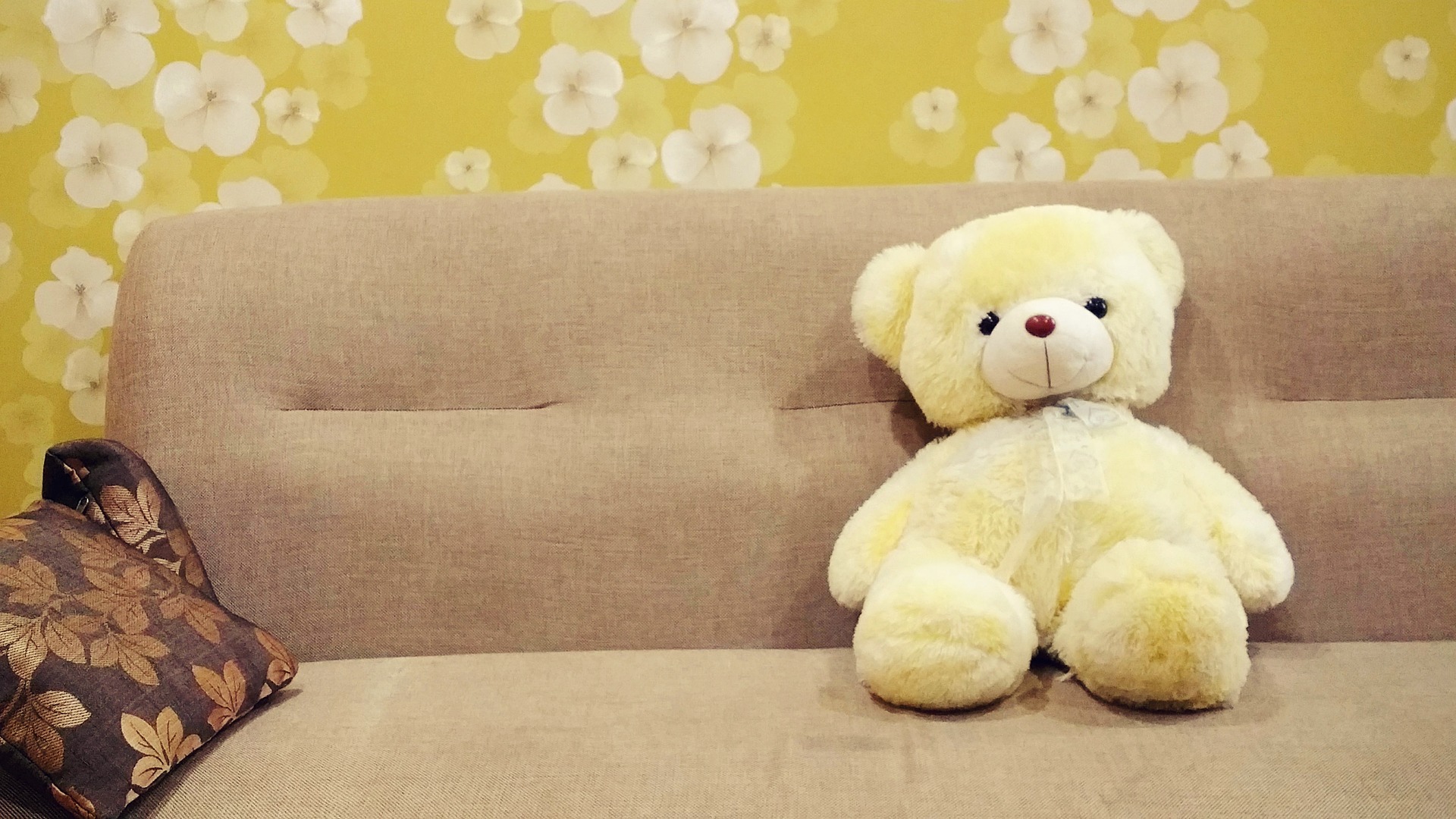 Urso de pelúcia amarelo em cima de uma sofá bege. A parede também é amarela. Imagem ilustrativa do texto sobre limpar sofá Sidil Divinópolis.
