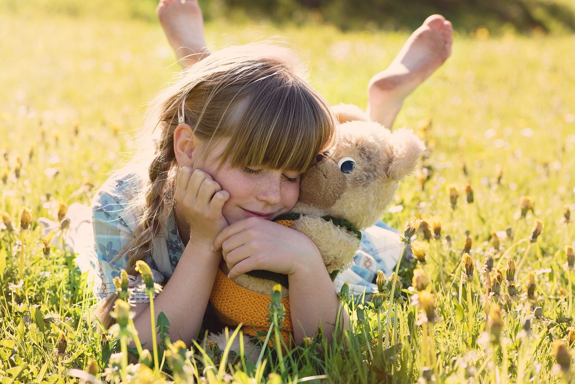 Foto de uma menina em um lugar com grama, abraçada com um urso de pelúcia. Imagem ilustrativa para o texto desinfetar bichinhos de pelúcia.