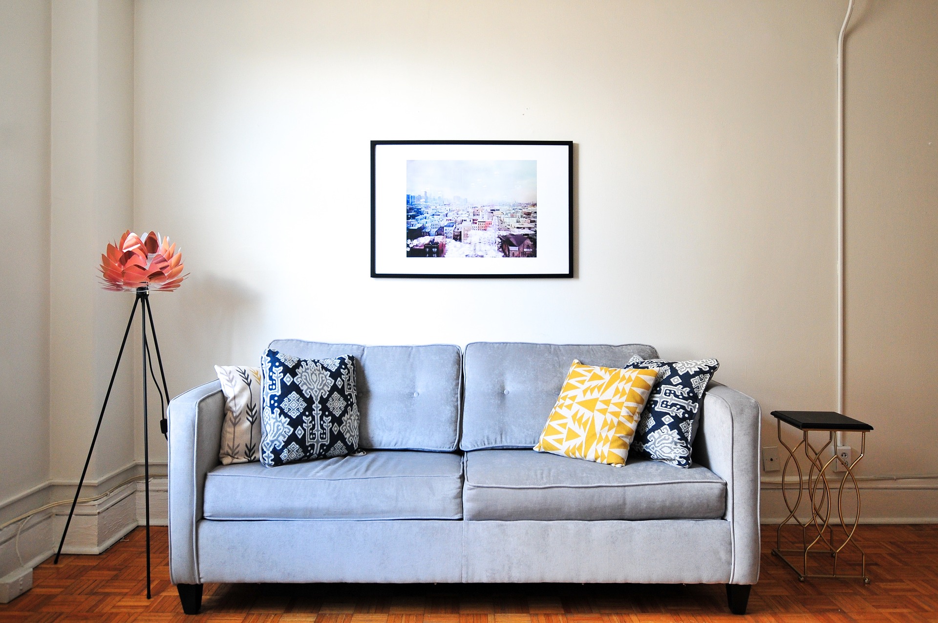 Sofá claro de dois lugares com almofadas nos cantos. Ao fundo uma parede branca e um quadro. Imagem do texto sobre limpar sofá em Ipatinga.
