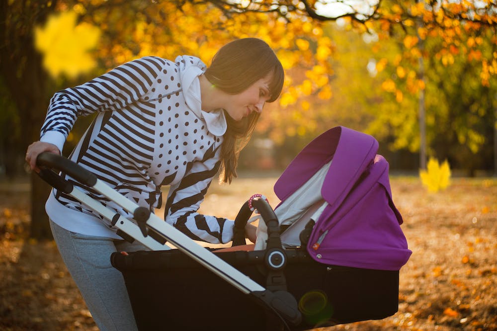 Mãe sorridente, olhando bebê, dentro de carrinho com detalhe roxo. Ilustração do texto sobre higienização de carrinho de bebê.