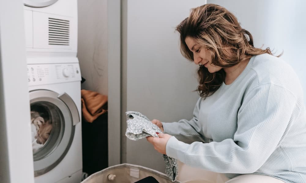 Mulher de camisa cinza observa manchas nas roupas lavadas. Imagem ilustrativa texto tirar tinta de caneta da roupa.