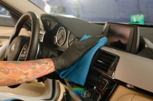 Mão masculina, usando luva preta, limpado interior de veículo. Ilustração do texto sobre limpeza interna do carro.