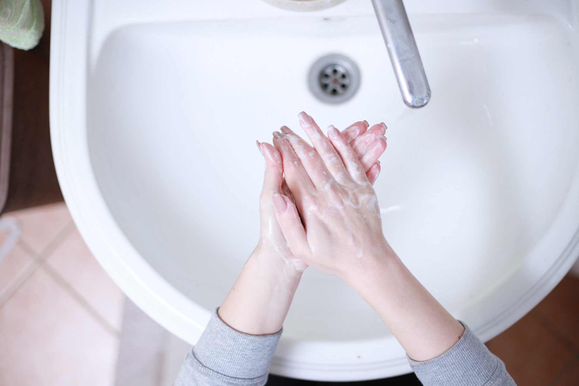 Foto de uma pessoa lavando as mãos em uma pia branca. Imagem ilustrativa para o texto pandemia.