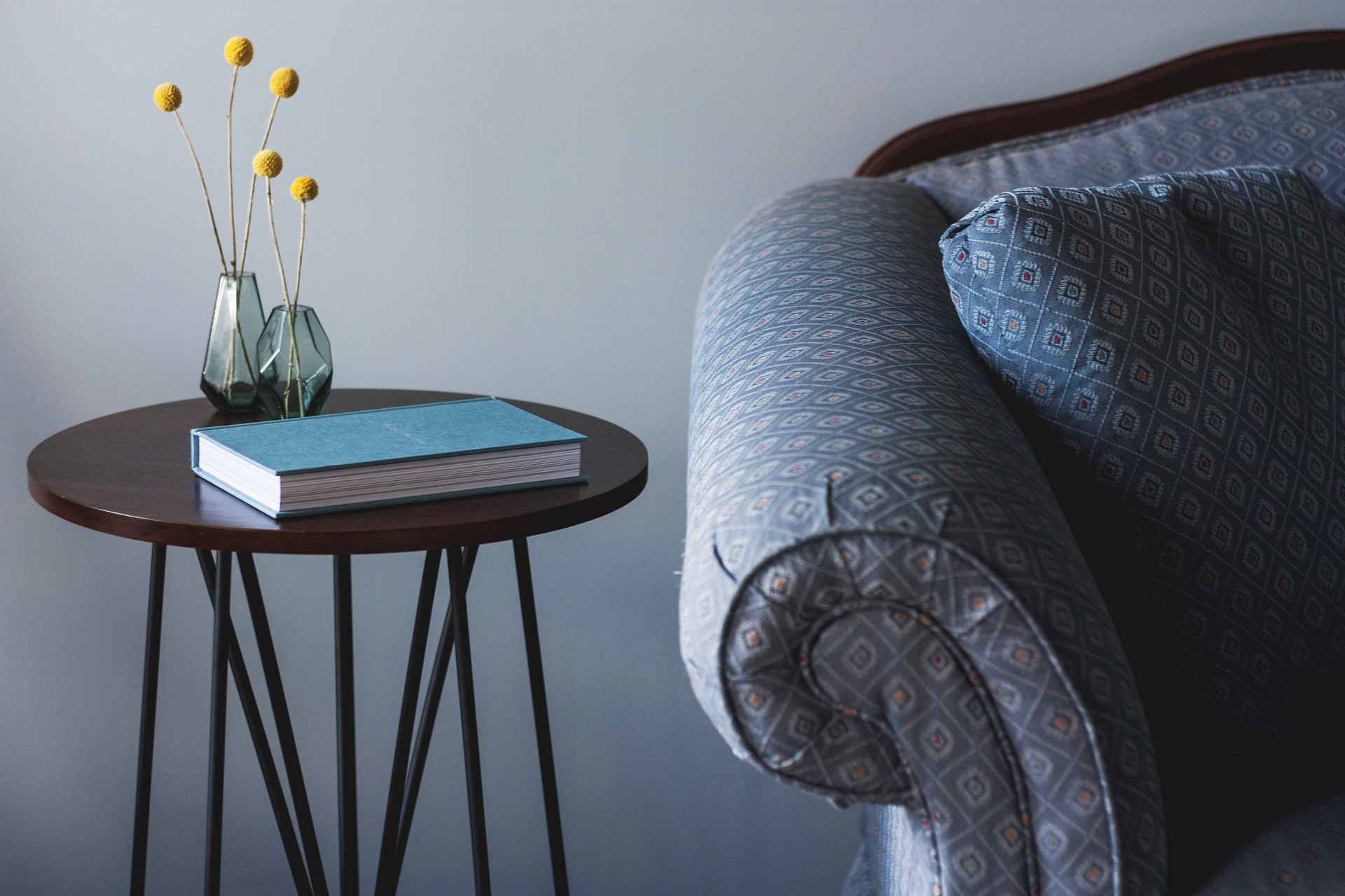 Imagem de um braço de sofá cinza ao lado de uma mesa com um livro azul em cima. Ilustrativa do texto sobre limpar sofá no Batista Campos.
