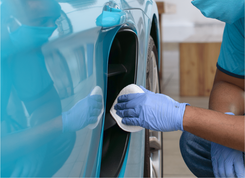 Mão de um homem com luva e camisa azul, polindo a lataria de um carro na mesma cor. Imagem ilustrativa para o texto lavar carro no Shopping Raposo.