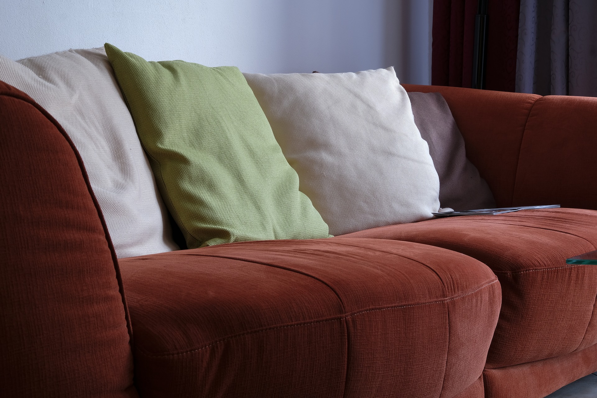 Sofá vinho com asmofadas brancas e verdes. Imagem ilustrativa do texto lavar sofá no Plano Piloto.