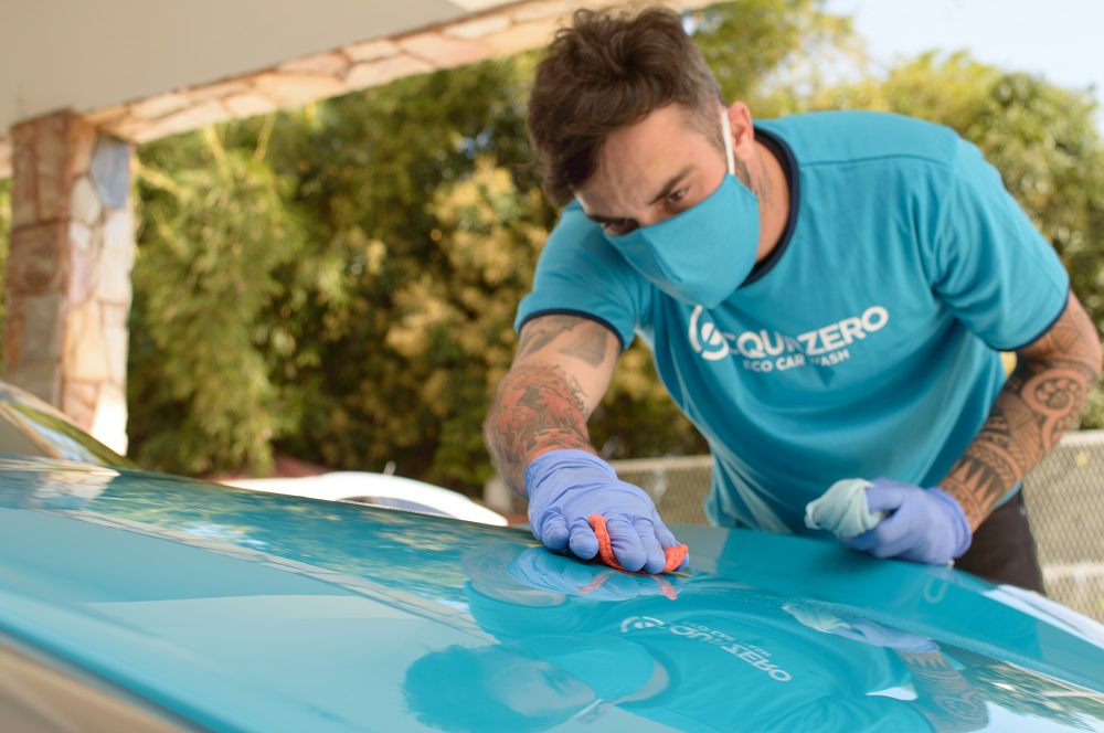 Foto de um funcionário da franquia Acquazero limpando um carro azul. Imagem ilustrativa para o texto faturamento de uma franquia Acquazero.