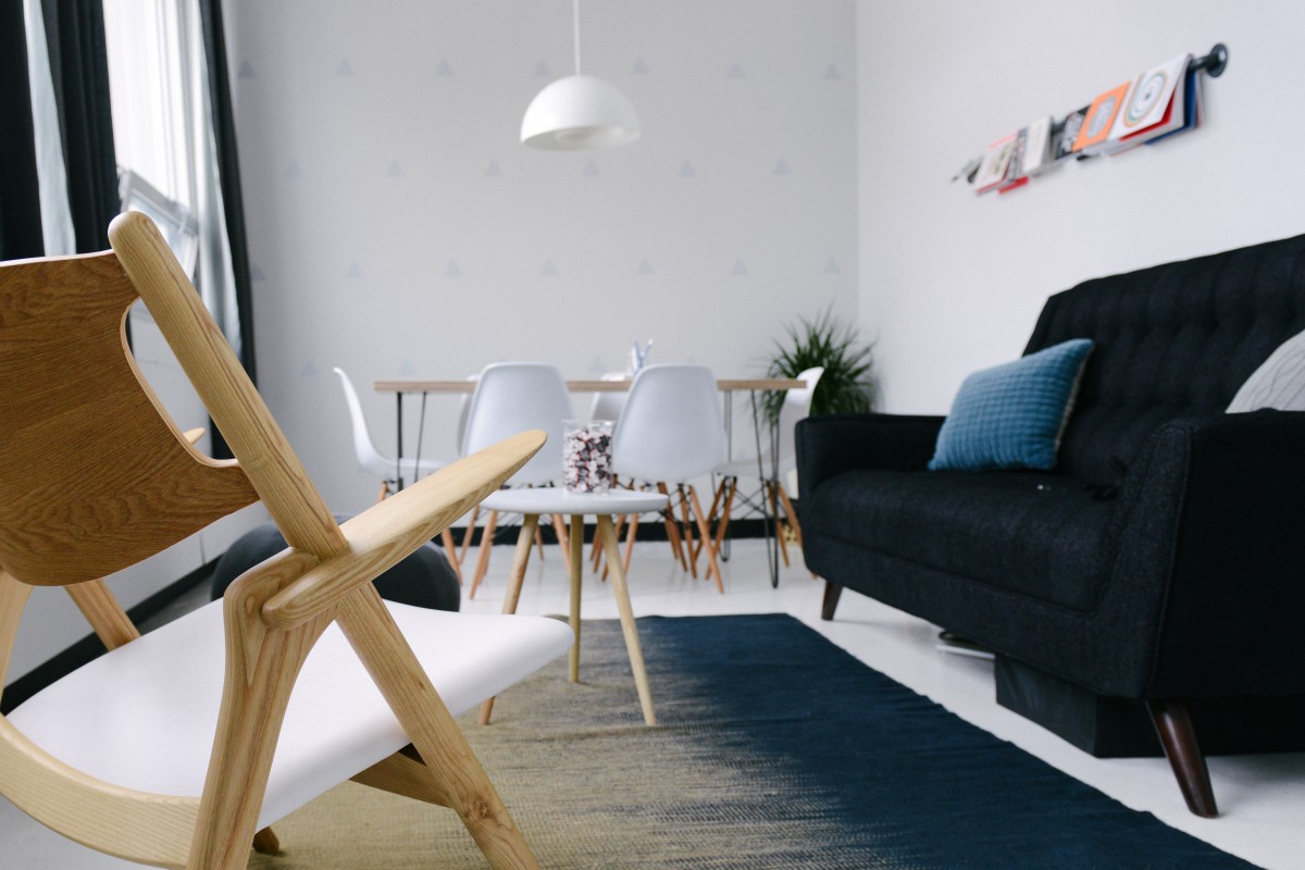 Sala com cadeiras brancas de madeira, parede e luminária brancas, sofá e tapete azuis. Imagem ilustrativa do texto lavar sofá no Centro de Barueri.