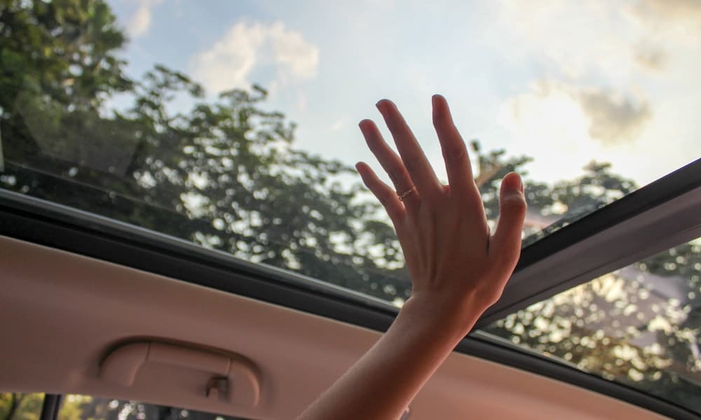 Mão feminina toca o vidro do teto solar do carro. Imagem ilustrativa texto limpar vidro.