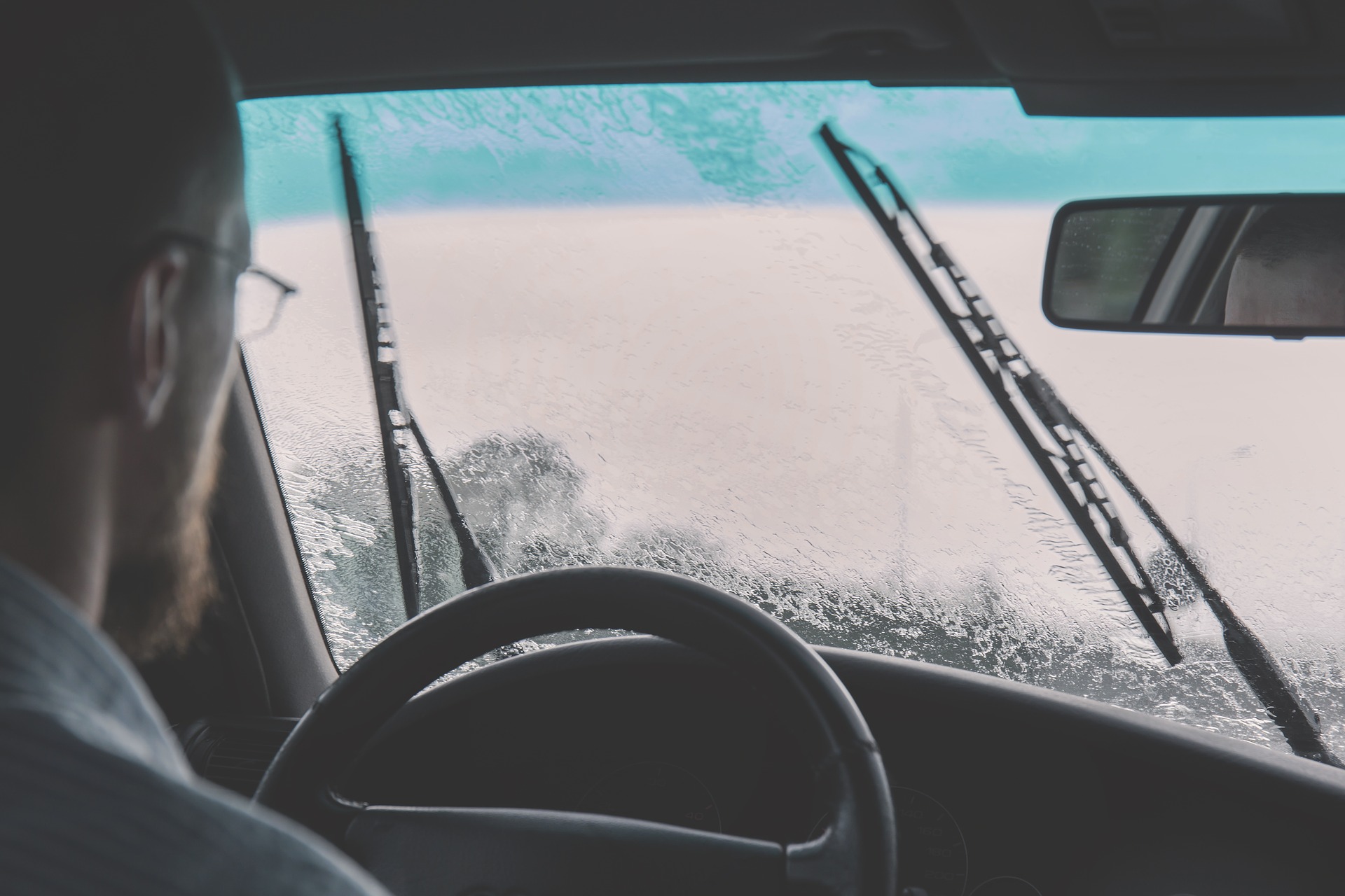 Foto de um homem dirigindo um carro na chuva. Imagem ilustrativa para o texto remoção de chuva ácida.