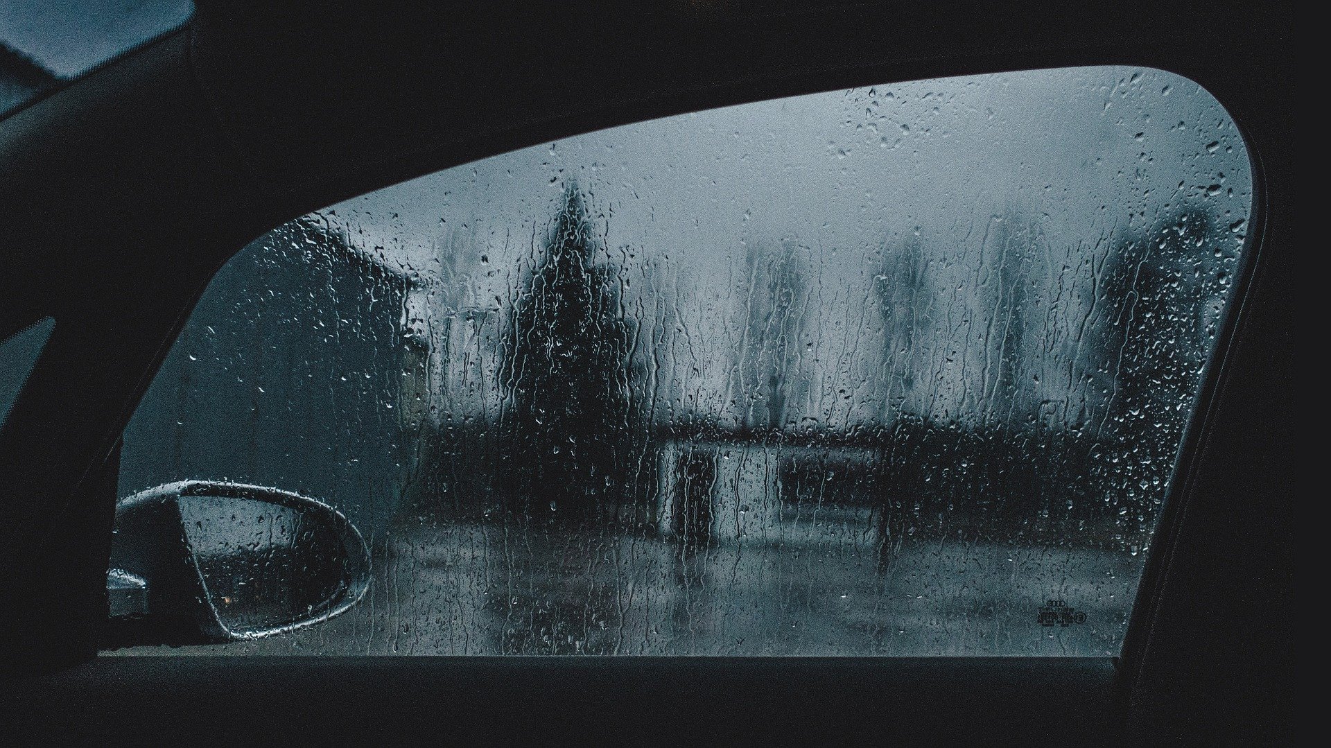 Foto da janela de um carro em noite de chuva. Imagem ilustrativa para o texto remover manchas de chuva ácida do vidro.