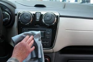 Mão masculina limpa painel do veículo com uma flanela cinza. Imagem ilustrativa texto chato com carro.